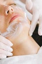 From above of crop faceless cosmetician applying facial mask on customer face during cosmetic procedure in modern spa salon